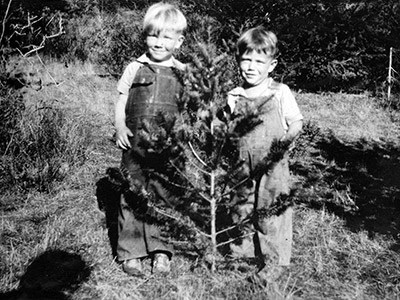 Two young boys standing in back of a sapling