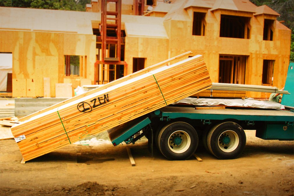 Truck unloading large stack of wood.