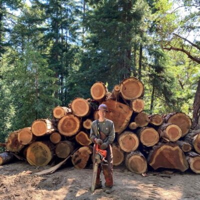 Man in logging gear in front of logs