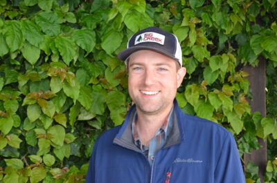 Man with hat standing, smiling in front of plants
