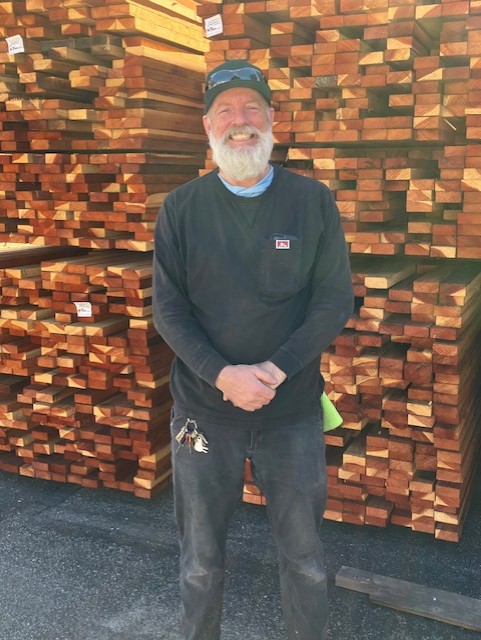 Man with a beard standing in front of a stack of lumber