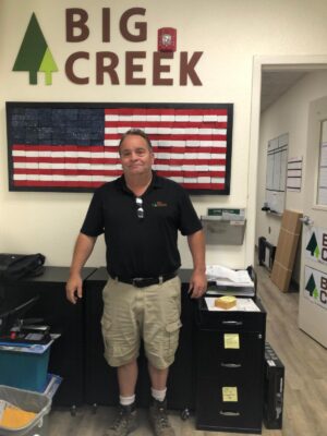 Man standing in front of wall that says big creek on it with an American flag behind him