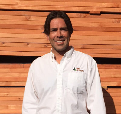 Man smiling in front of stack of wood