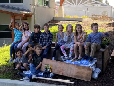 Kid's sitting with lumber and a garden bed grant donation