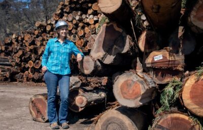 Photo of woman in a hard hat in front of a stack of logs