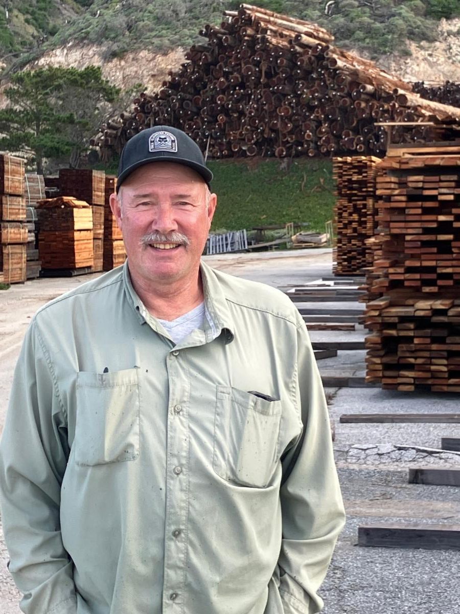 Man with hat standing in front of log pile