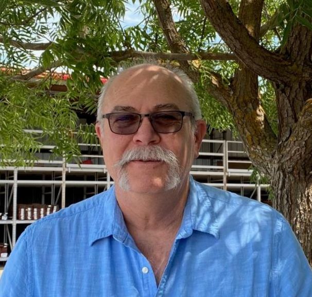 Man with blue shirt, glasses and mustache in front of tree