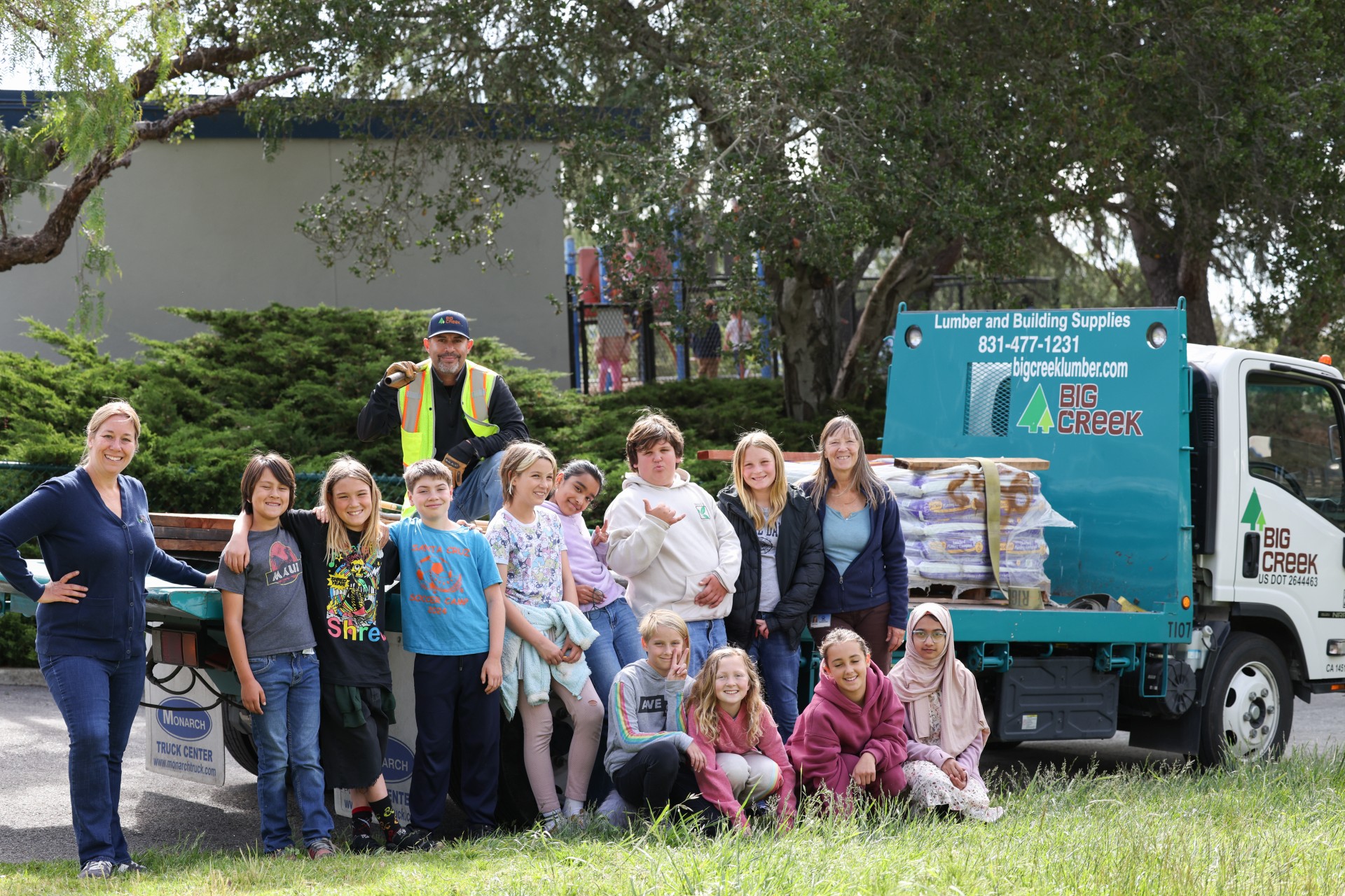 Kids, teacher and big creek lumber staff with delivery truck with soil and school garden bed grant materials
