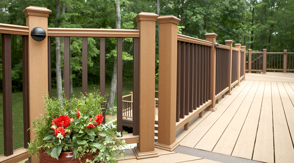 A composite deck with handrails next to plants, flowers, and trees.