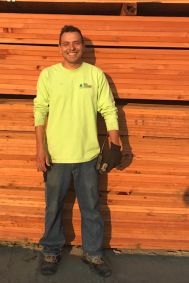 Man in yellow shirt standing in front of lumber.